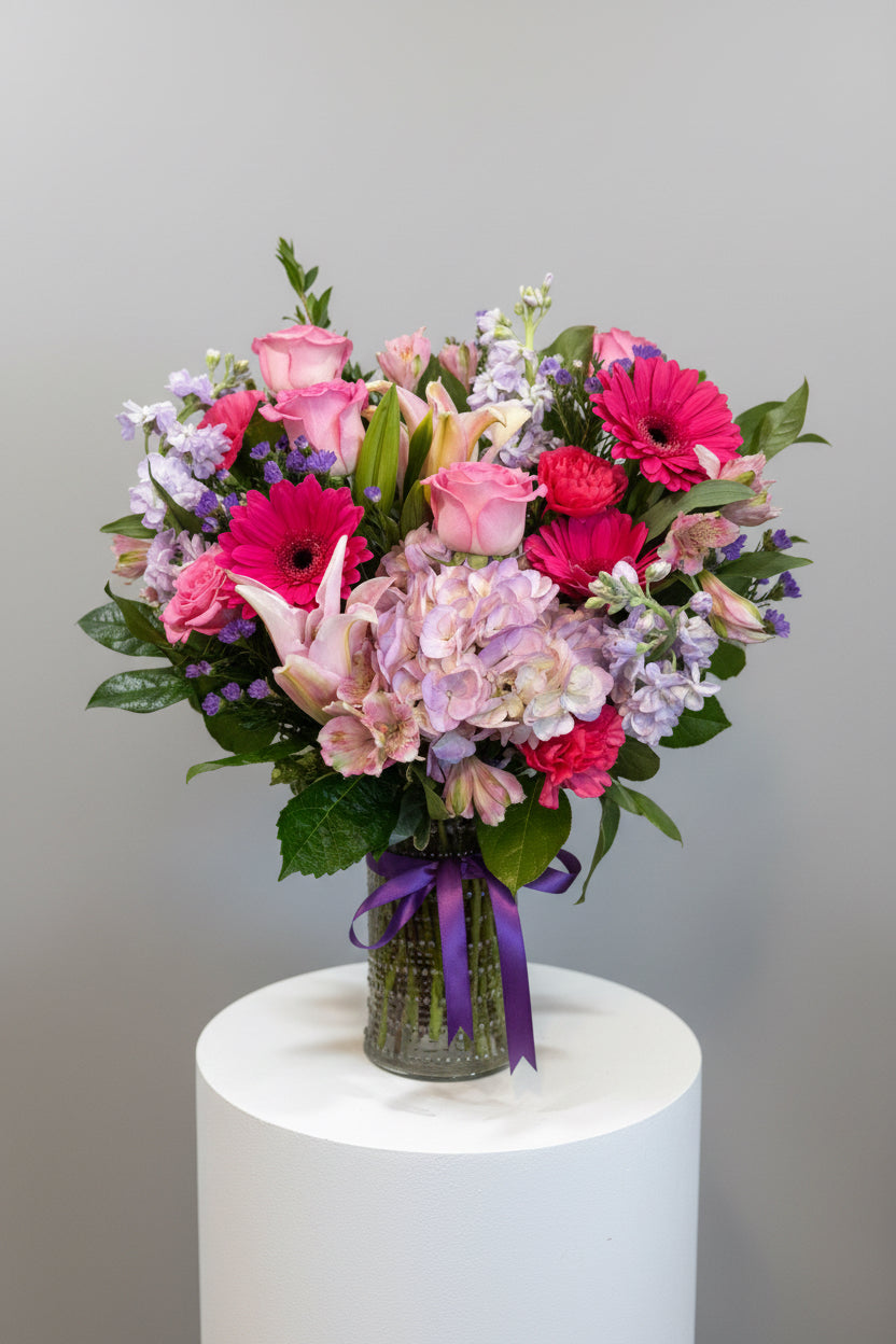 A vibrant mixed flower bouquet featuring pink roses, magenta gerbera daisies, light purple hydrangeas, lavender stock and green foliage, 