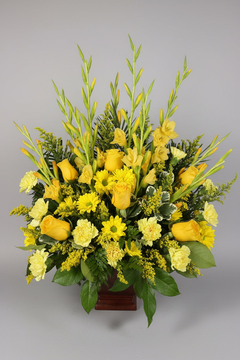 A vibrant yellow and green floral arrangement featuring yellow roses, gladiolus, daisies, and green foliage