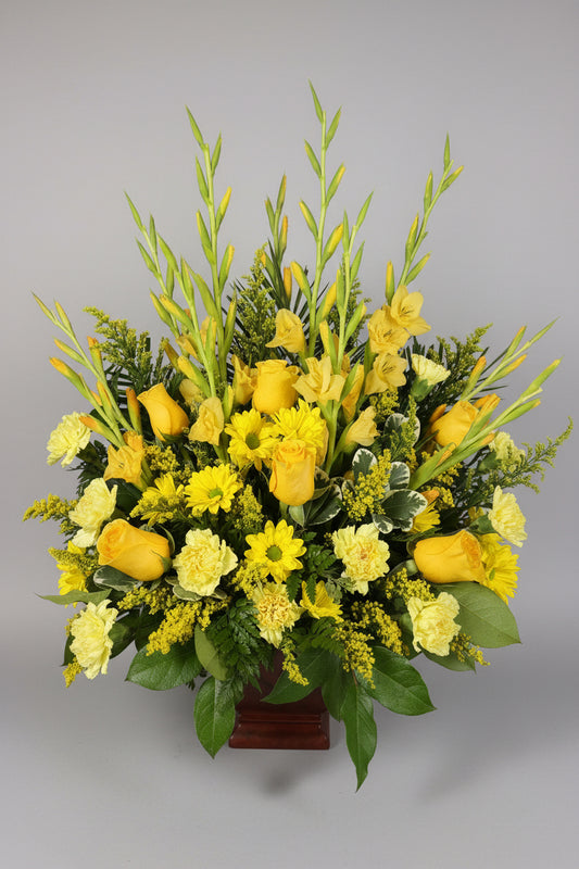 A vibrant yellow and green floral arrangement featuring yellow roses, gladiolus, daisies, and green foliage