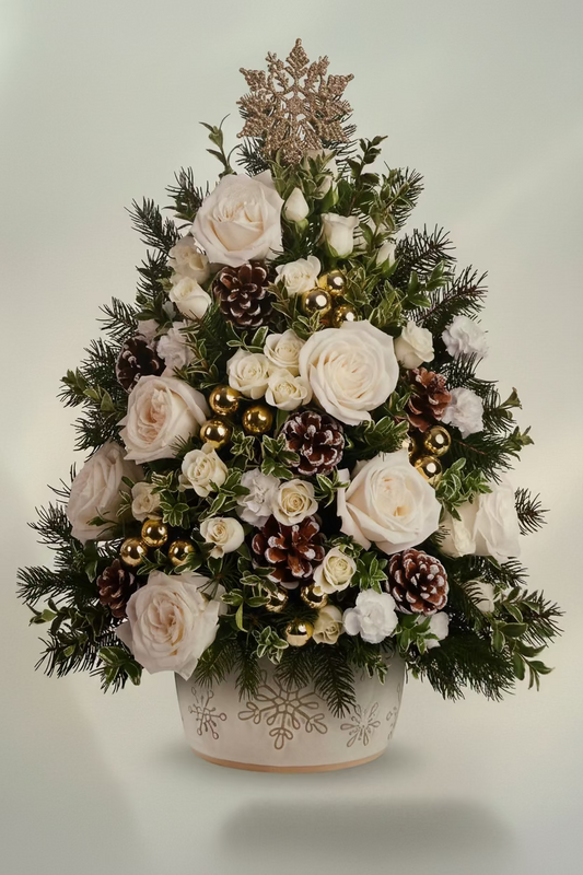 Telefona's Snowy Oakis Tree floral arrangement in a white pot with gold snowflake details, featuring white roses, green pine branches, brown pinecones, gold ornaments, and a gold star topper, set against a light beige background.